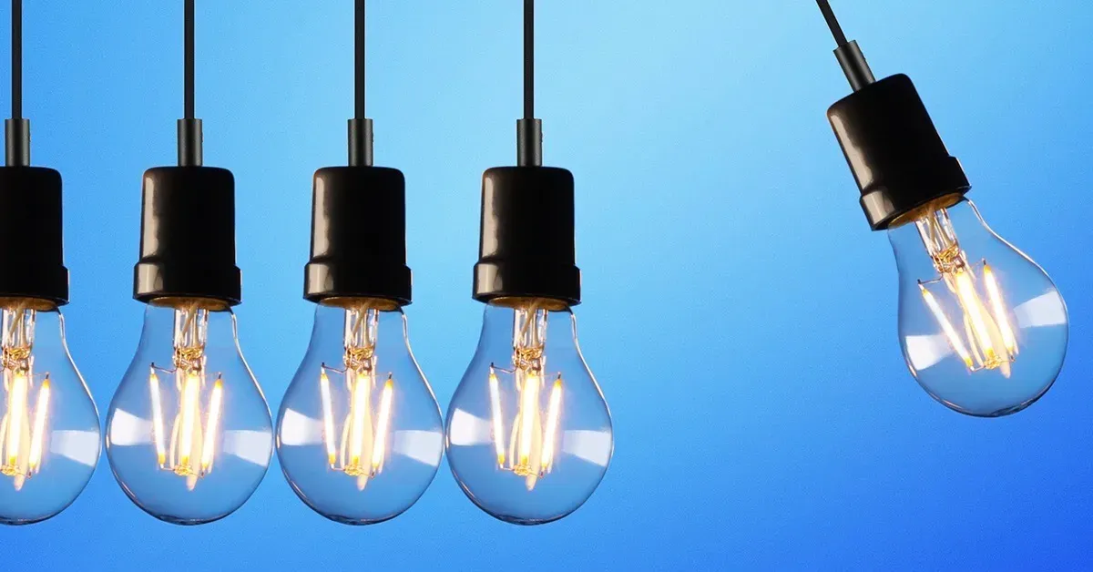 Række af tændte Edison-pærer hængende foran blå baggrund.
