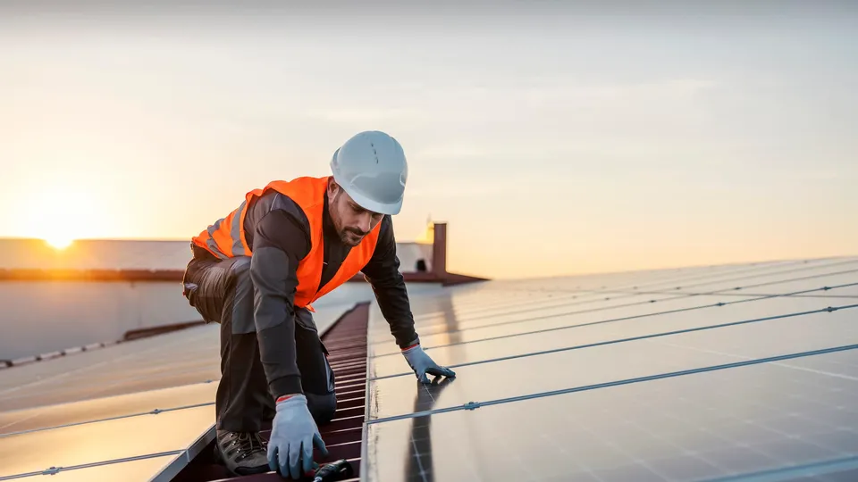 Trabajador instalando paneles solares en azotea al atardecer.