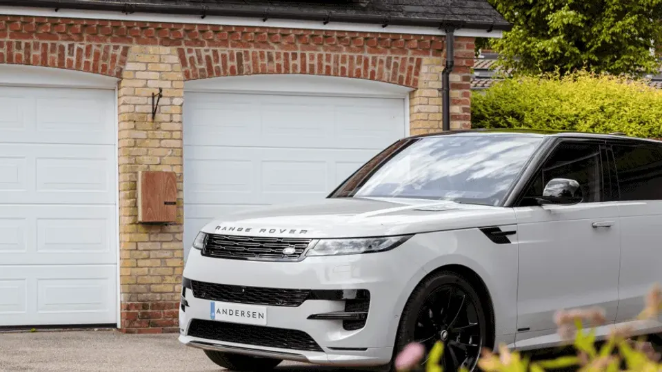 White Range Rover parked outside a residential garage with a home EV charger mounted on the wall