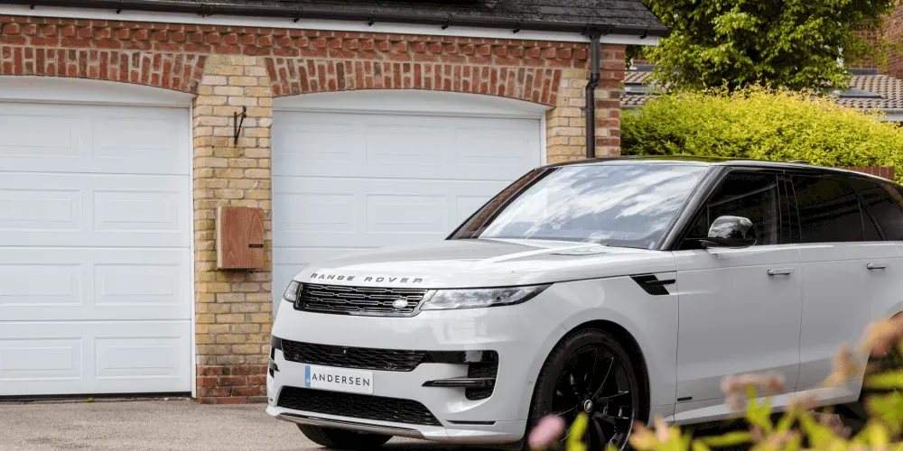 White Range Rover parked outside a residential garage with a home EV charger mounted on the wall