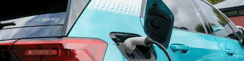 Electric vehicle charging cable plugged into turquoise car.