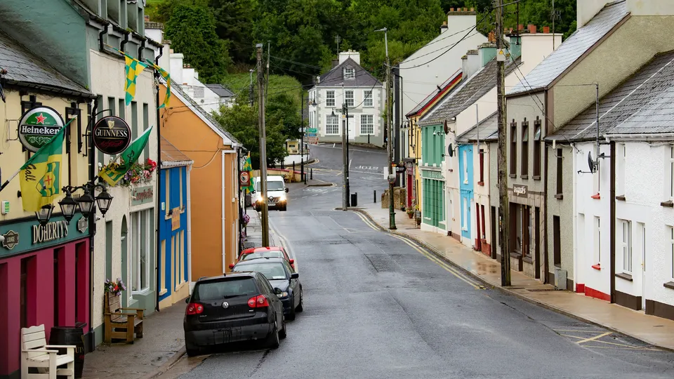 Colorful village street with parked cars and pub signs.