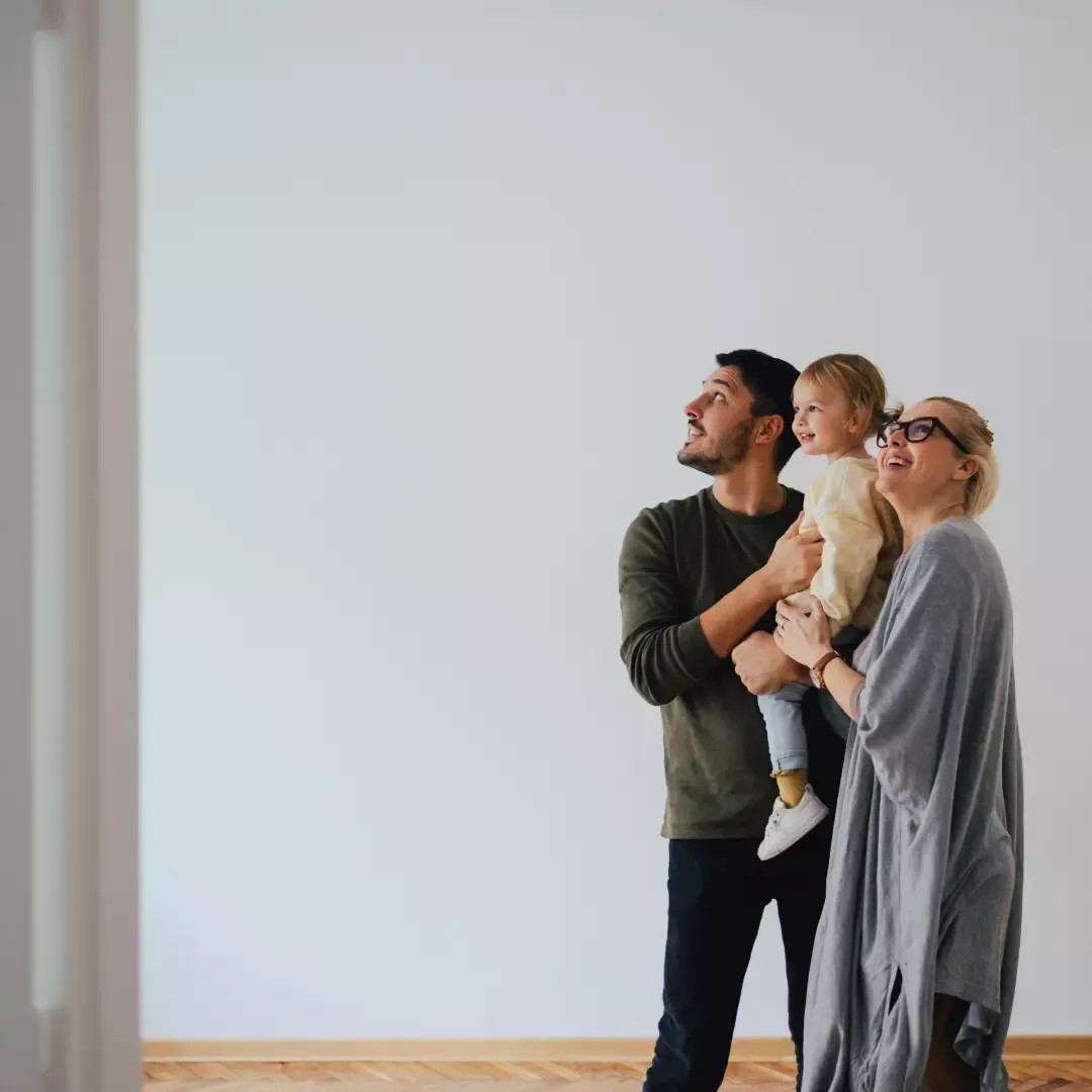 Familj på tre personer tittar uppåt tillsammans i ett tomt rum.
