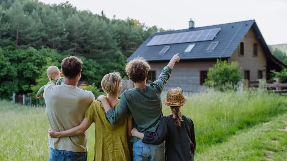 Familie mit fünf Personen steht auf Feld und blickt auf Haus mit Solarpanelen.