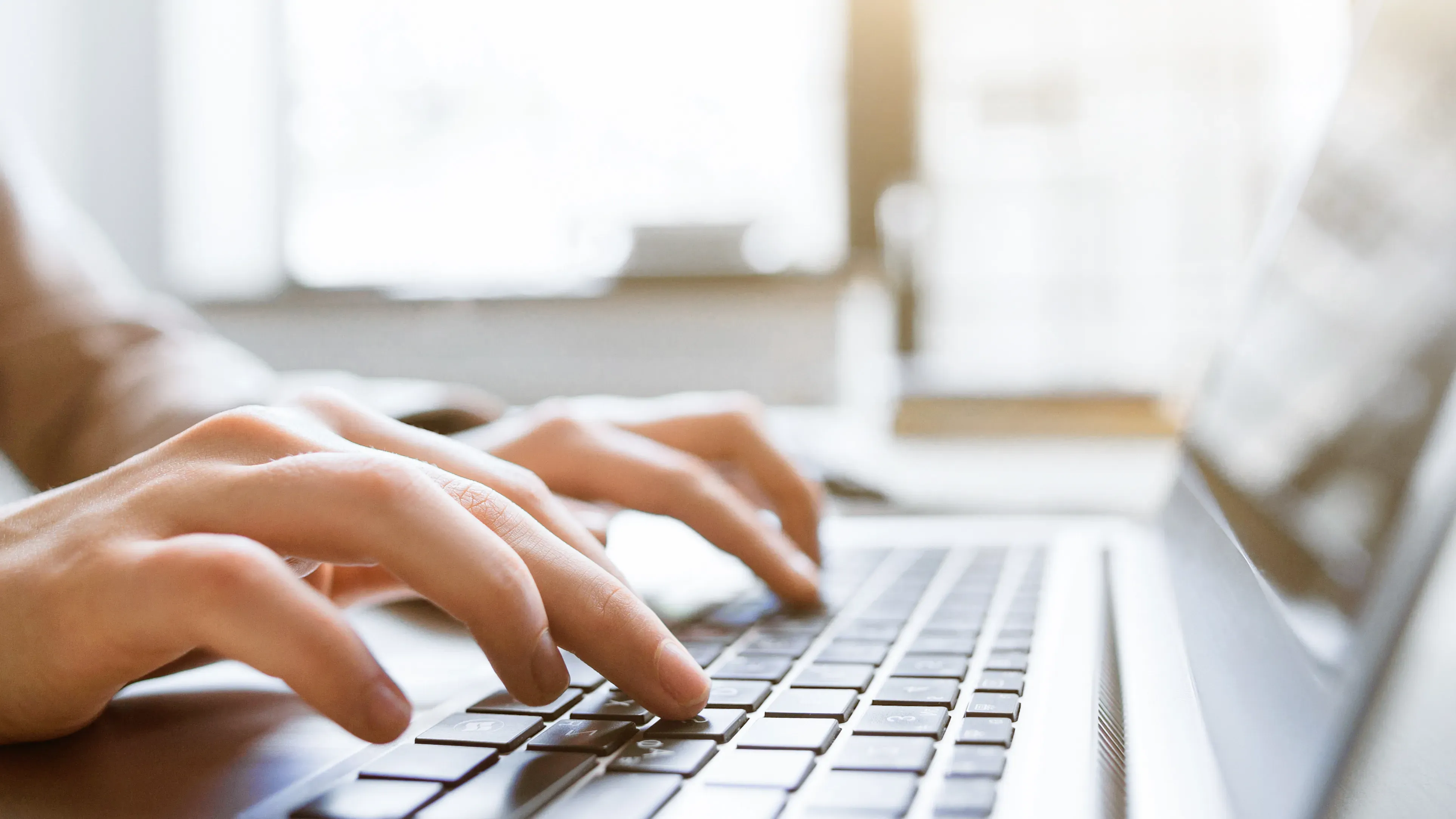 Person tippt auf Laptop-Tastatur am Schreibtisch.
