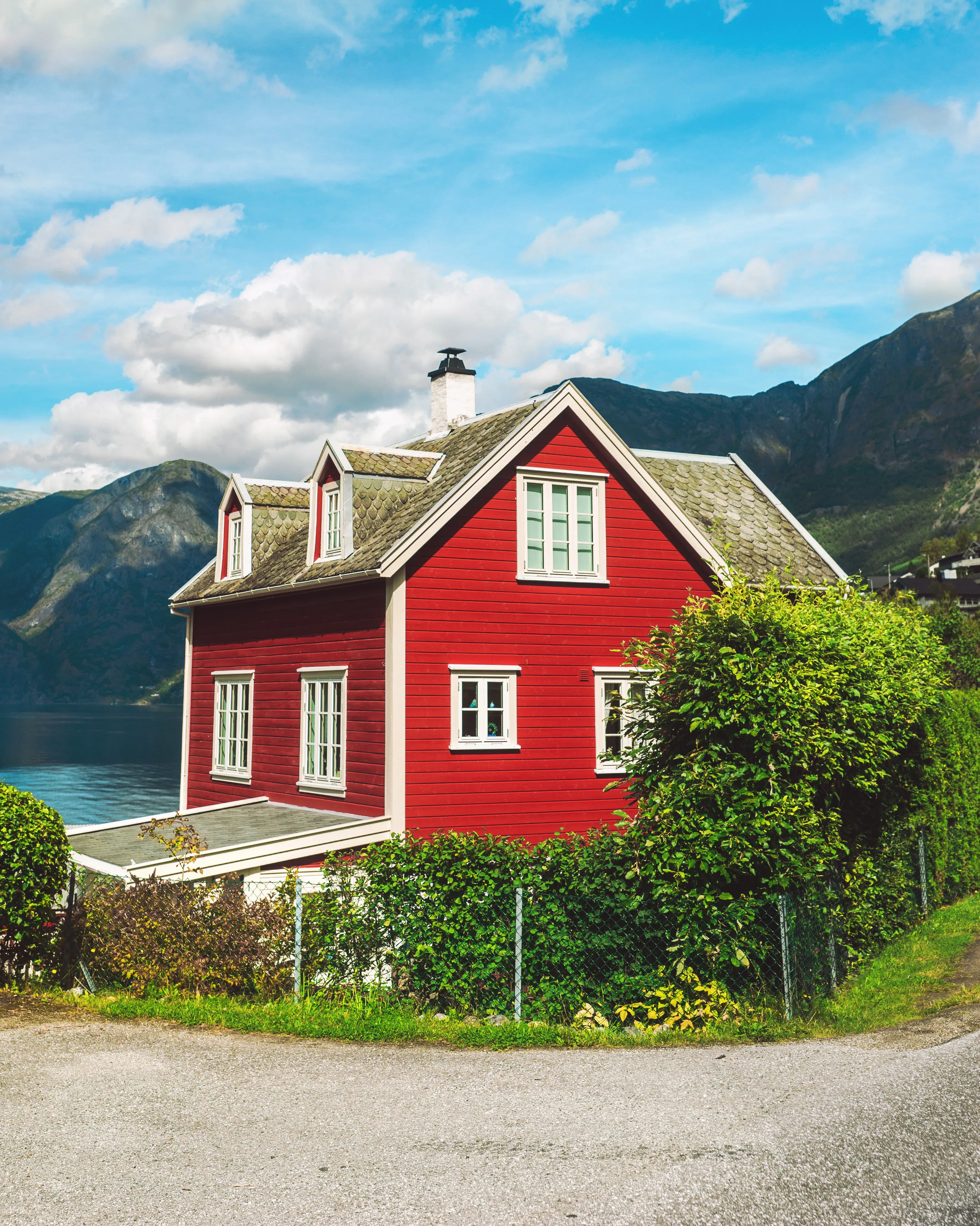 Rødt hus med hvit dekor og mosbedekt tak ved siden av en fjellsjø.