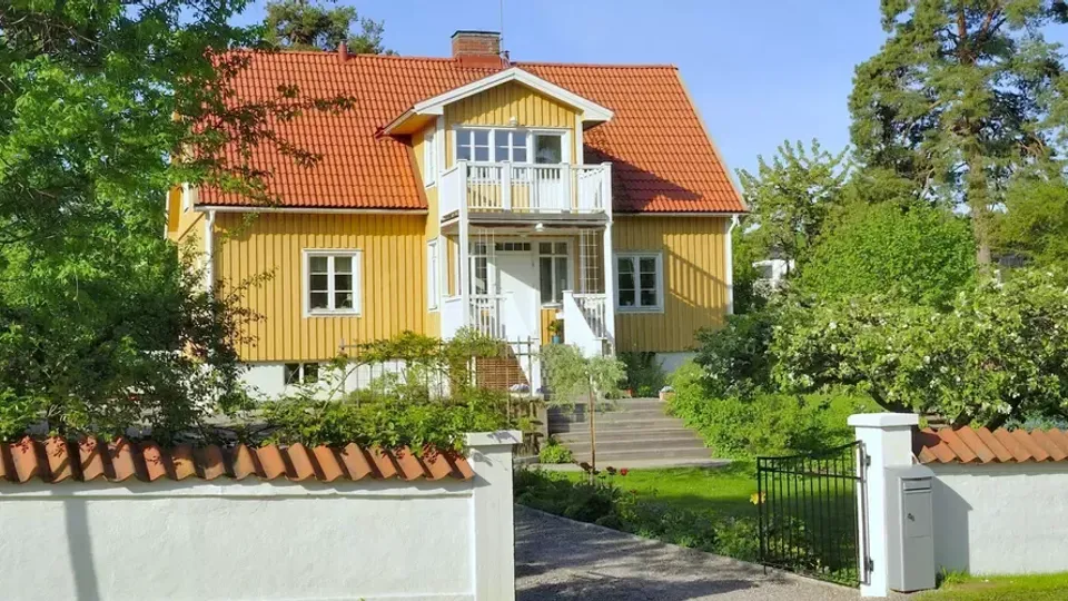 Gult hus med rött tak och vit list bakom vit staket.