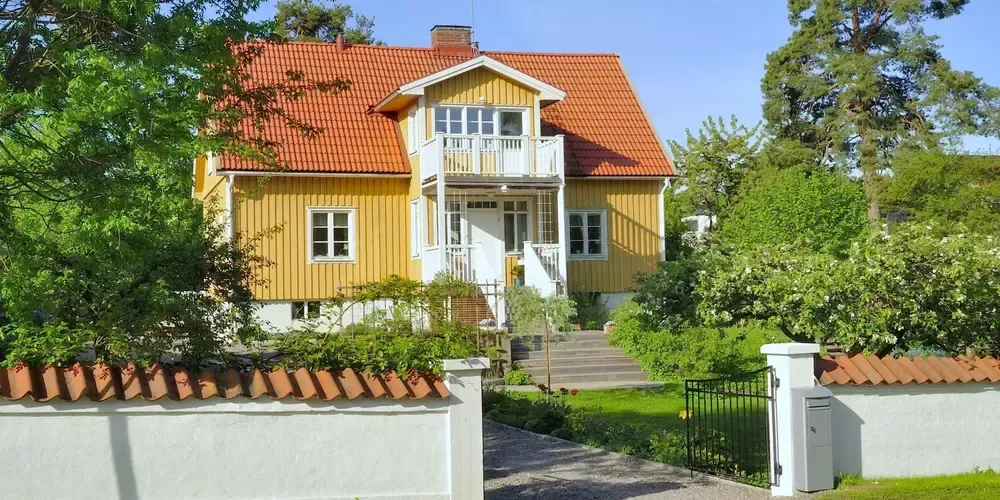 Gult hus med rött tak och vit list bakom vit staket.