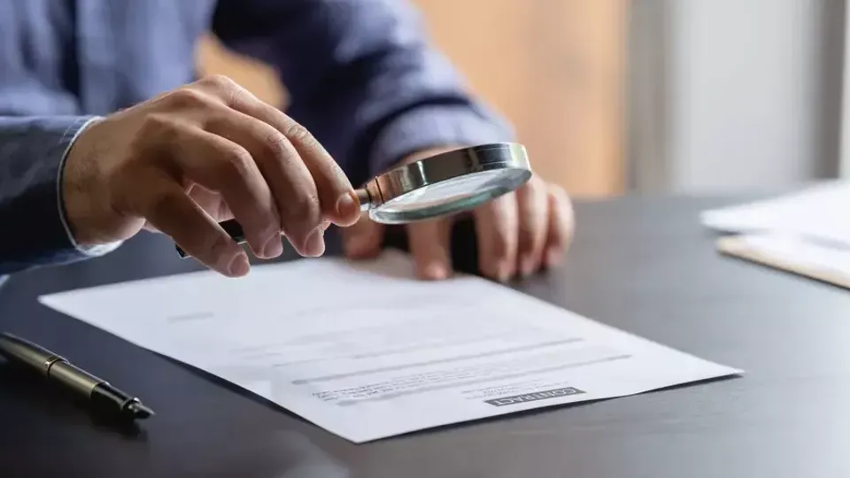 Person använder förstoringsglas för att granska dokument på skrivbord.