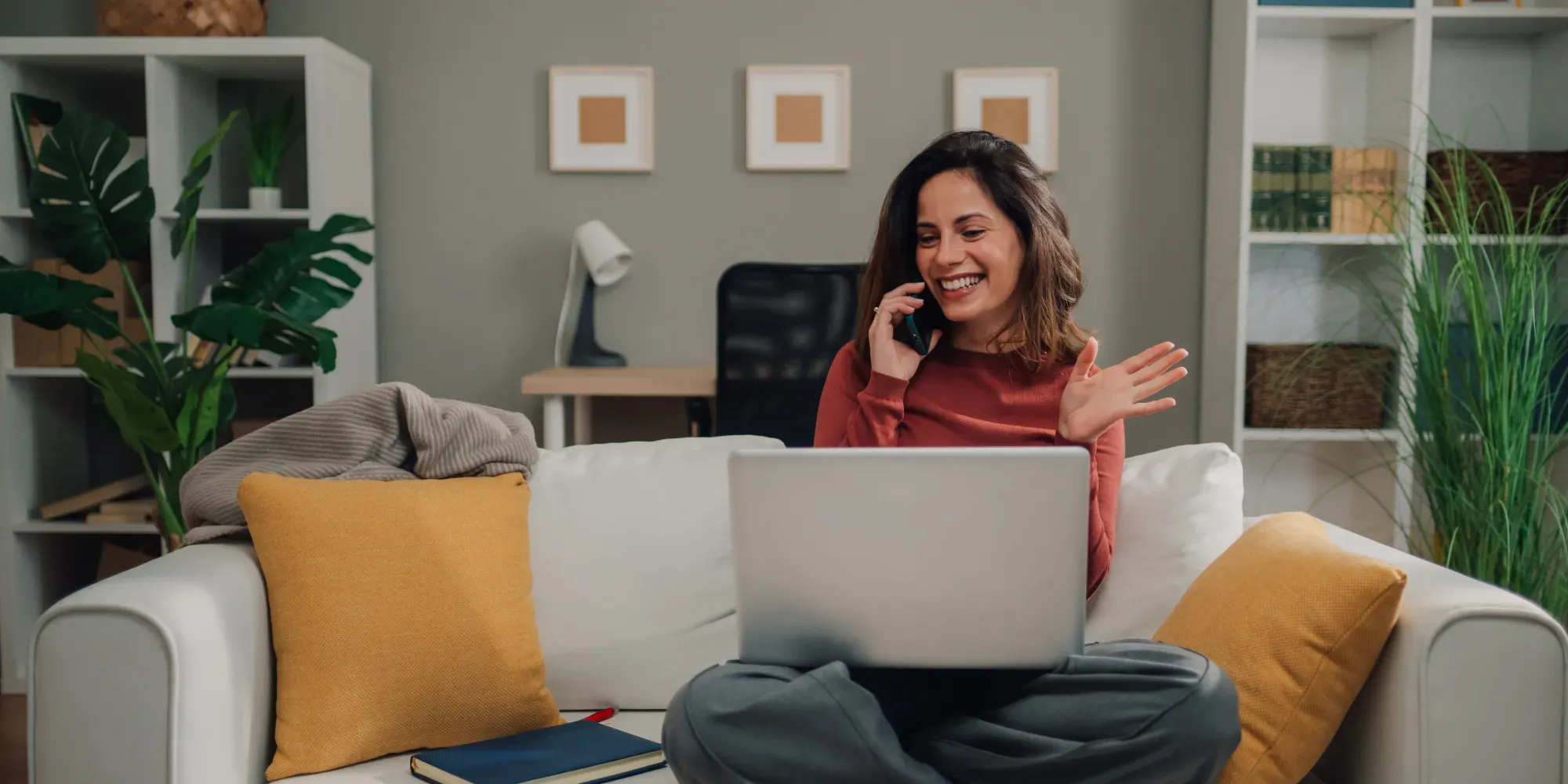 Mujer en sofá con portátil hablando por teléfono.