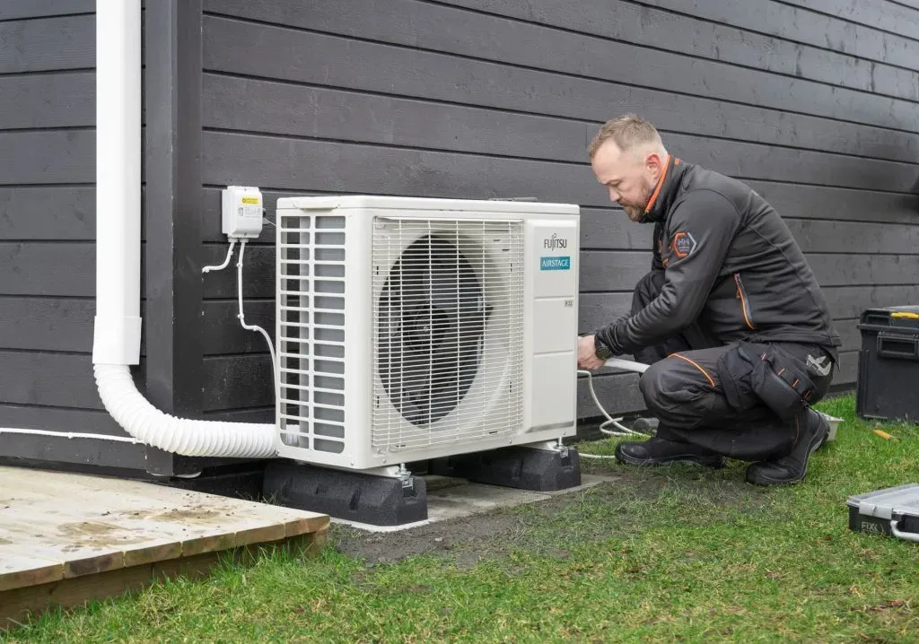 Tekniker servicerer udendørsdelen af en varmepumpe.
