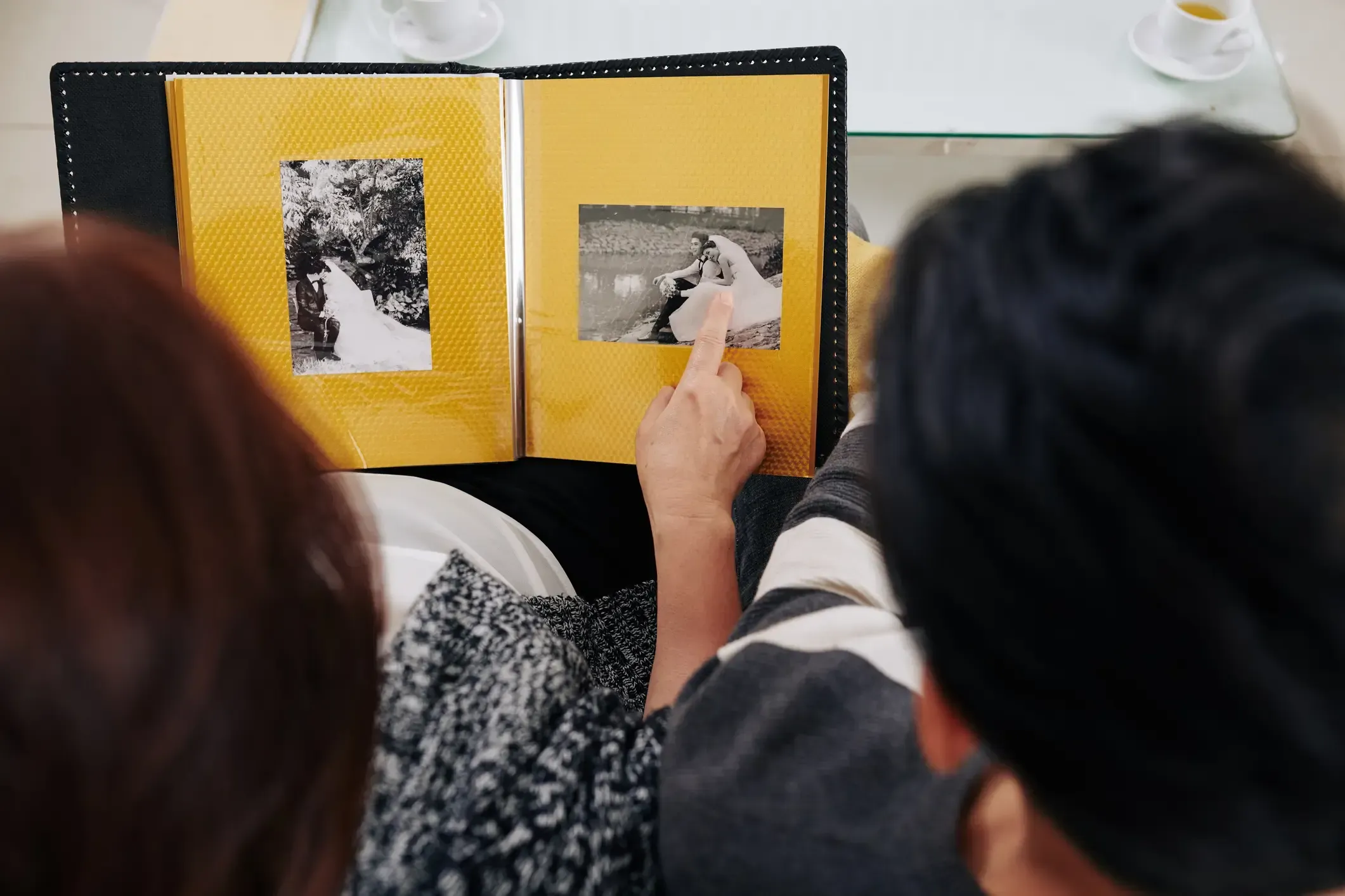Två personer tittar på ett fotoalbum med gula sidor och svartvita fotografier.