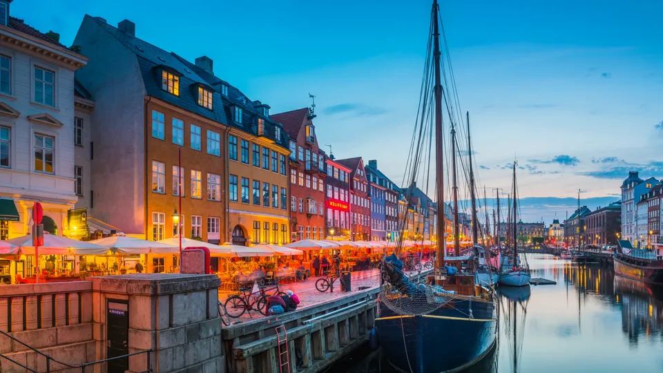 Nyhavn i Köpenhamn i skymningen, med färgglada hus, uteserveringar och segelbåtar längs kanalen.