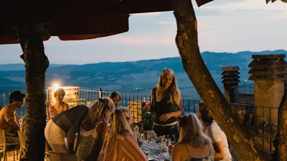 Grupp människor äter middag utomhus på en terrass med utsikt över kullriga kullar.
