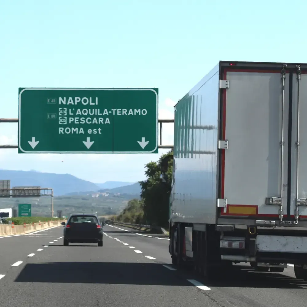 Flyttbil på motorväg i Italien med vägskyltar mot Rom och Napoli.