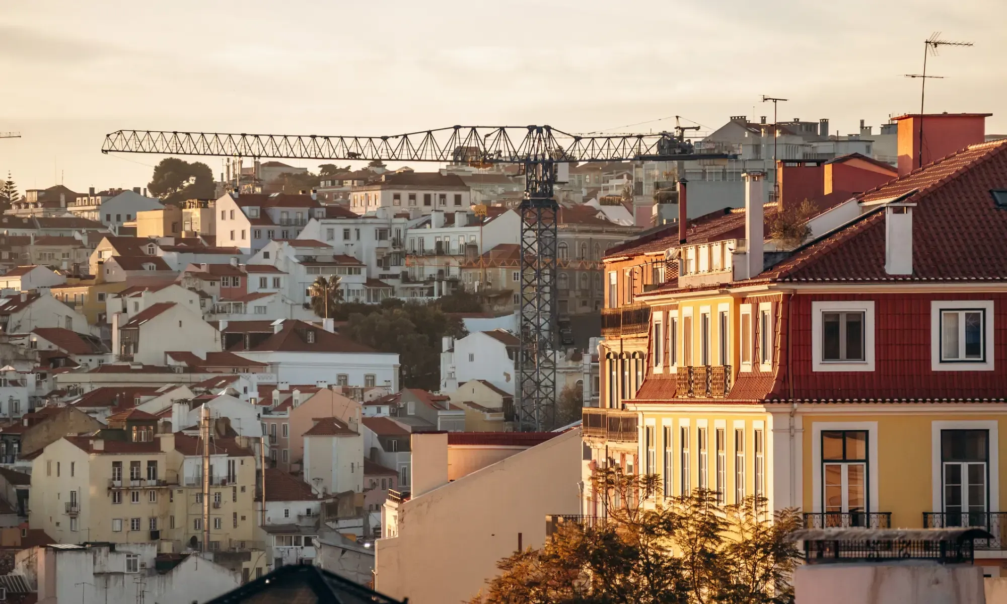 Utsikt över tätt byggda bostadshus med röda tak i Lissabon med en byggkran som reser sig över stadsbilden.