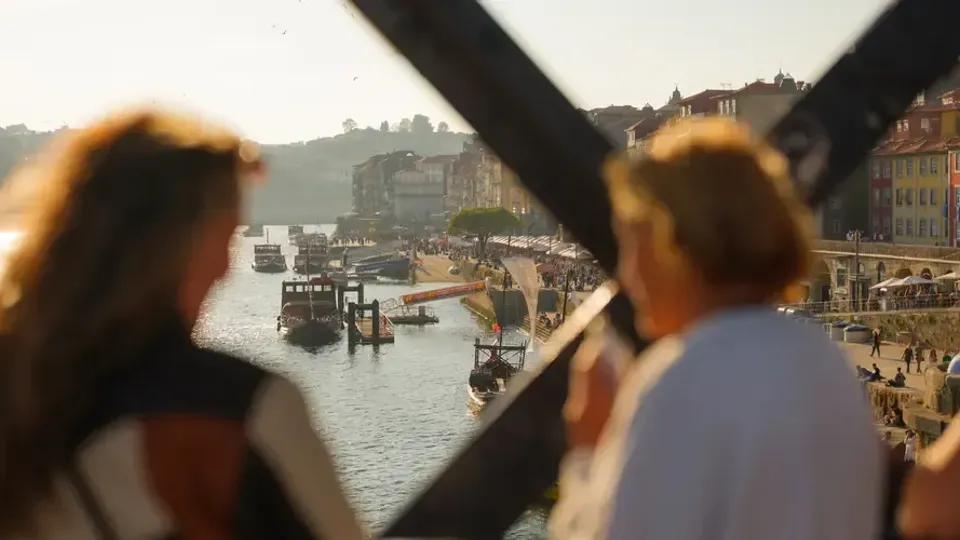 Två personer på en bro blickar ut över floden Douro i Porto, med båtar och färgglada hus i bakgrunden.