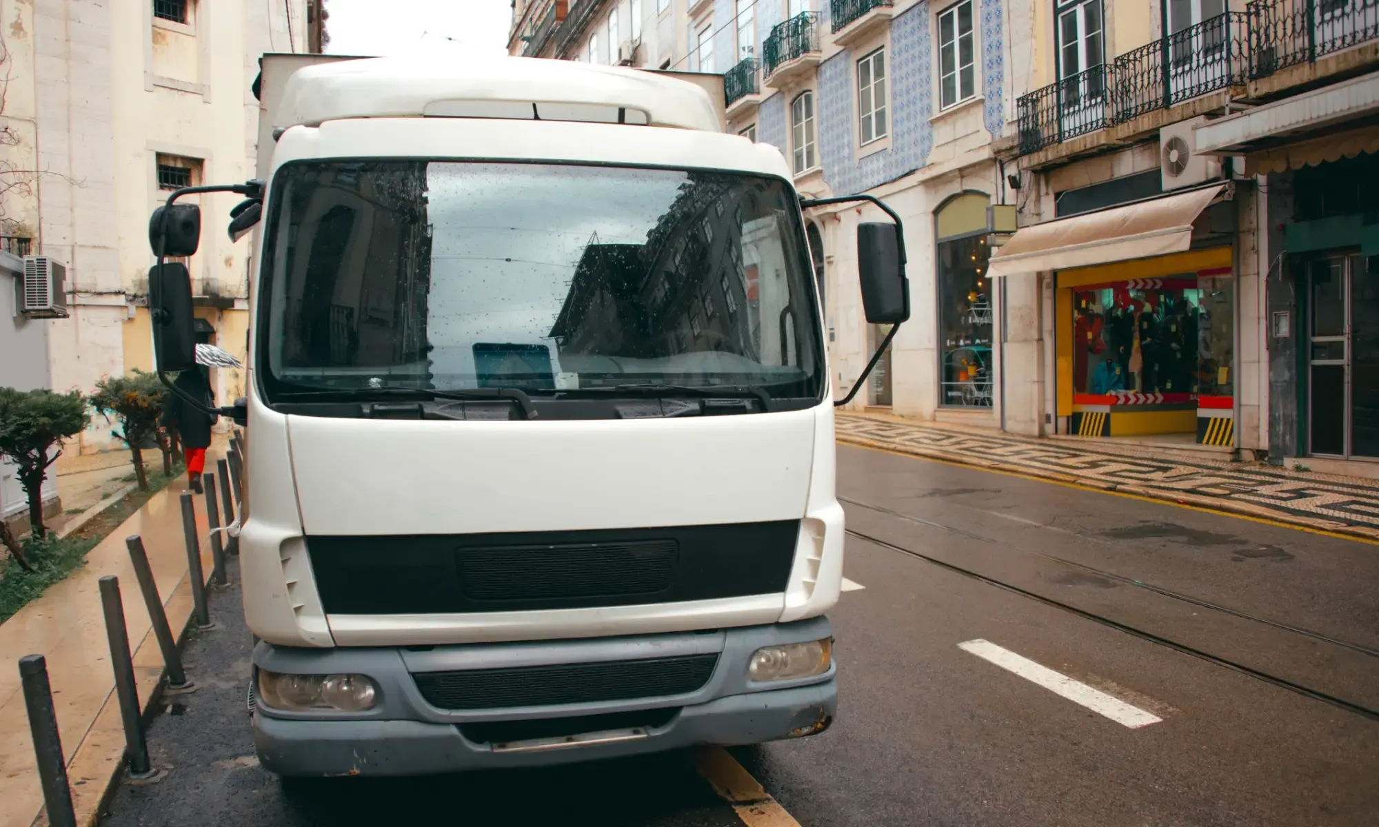 Vit flyttbil parkerad på en smal stadsgata med flerbostadshus och balkonger i en portugisisk stad.