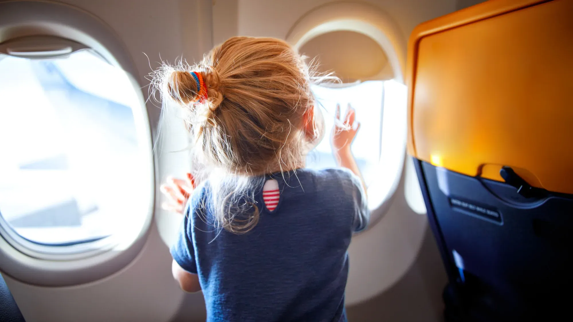 Blond flicka sitter och tittar ut genom flygplansfönstret.