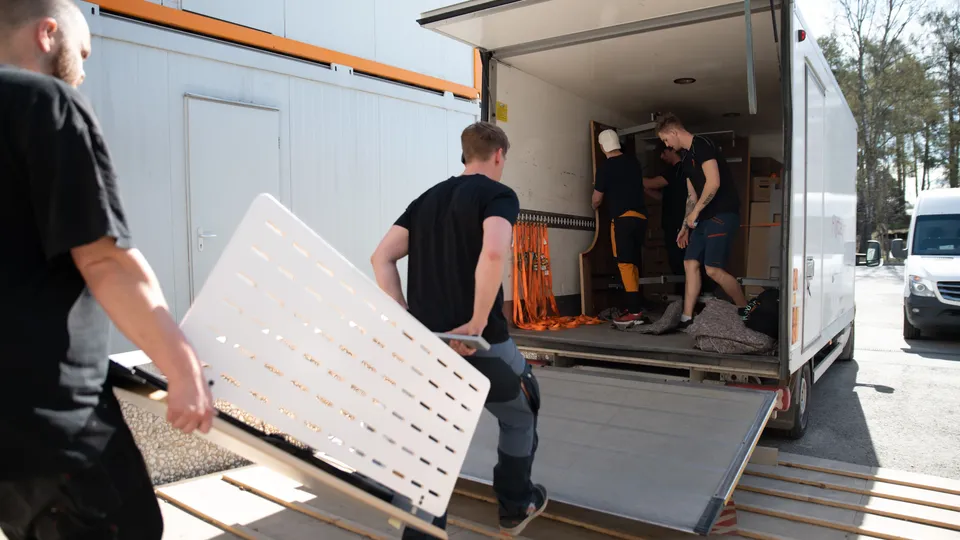 Arbeidere laster møbler og utstyr inn i en flyttebil.