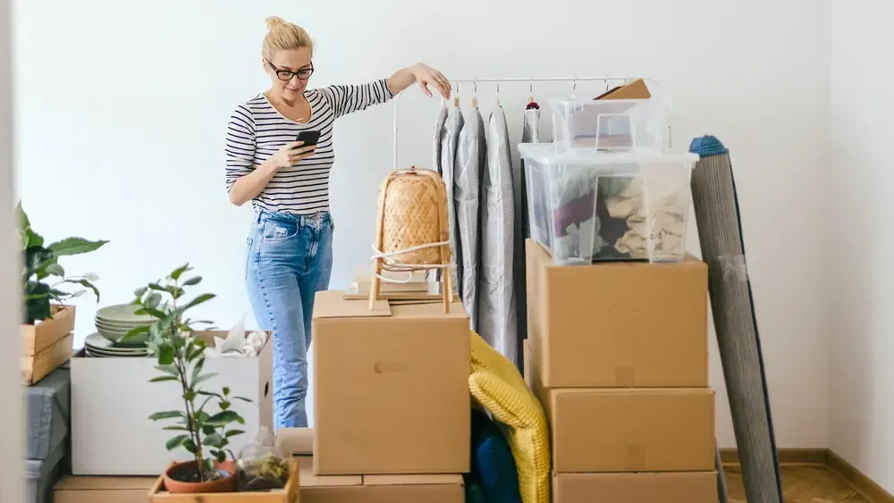 Kvinna som använder en smartphone bland packade flyttkartonger.