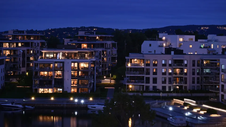 Opplyste vannkantleilighetsbygg i skumringen med fortøyde båter i forgrunnen.