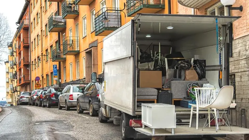 Flyttbil lastad med möbler och hushållsprylar parkerad på bostadsgata.