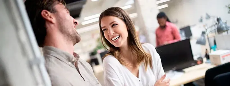 To kolleger smiler mens de taler sammen på et kontor.