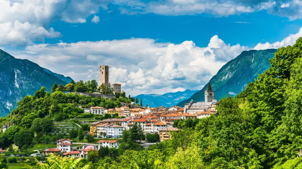 Torre medievale su una collina sopra un paese con montagne.