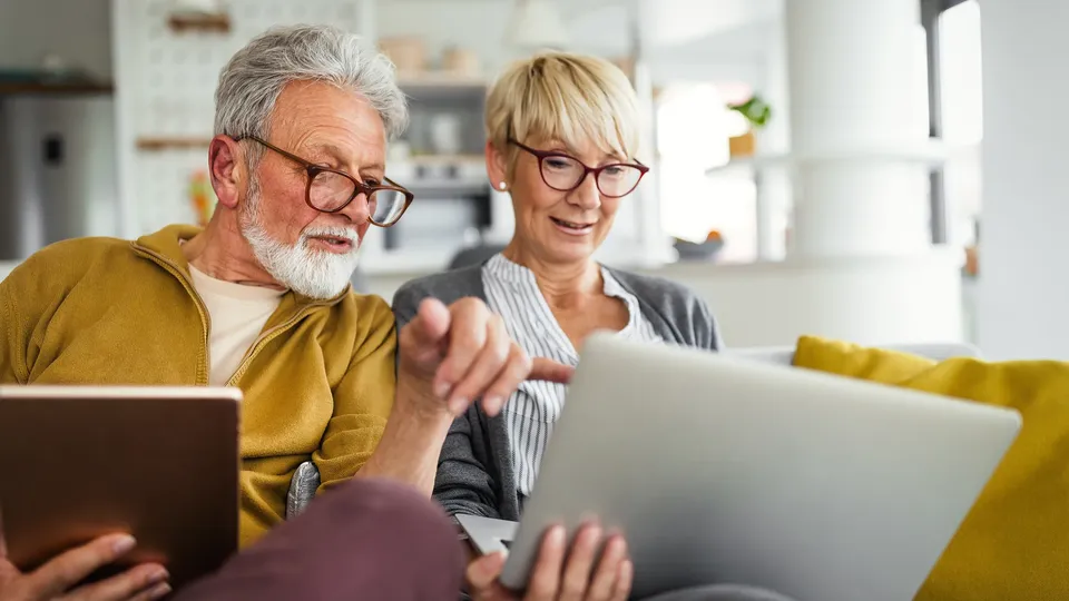 Ældre mand og kvinde ser på tablet sammen på sofa.