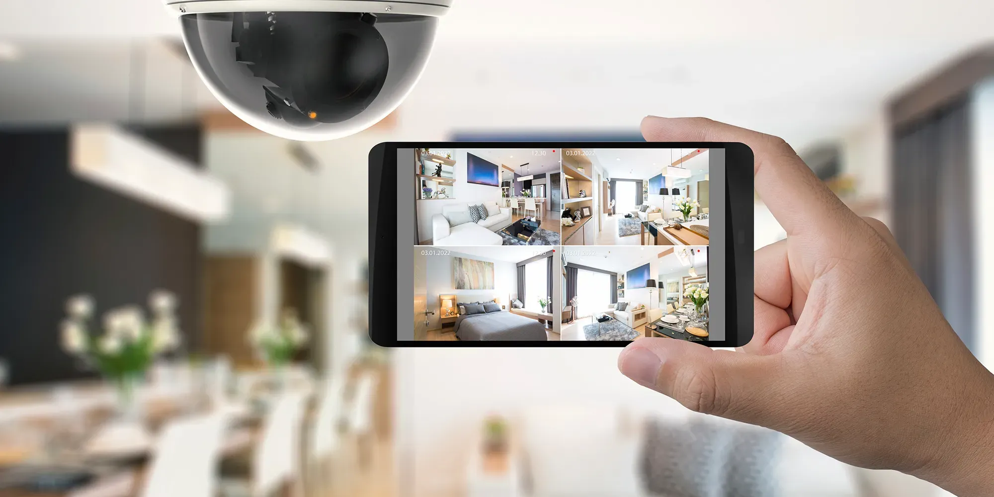 Hand holding smartphone displaying security camera feed with multiple room views.