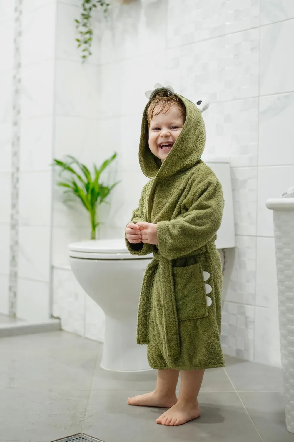 En glad liten kille står i badrummet bredvid toaletten.