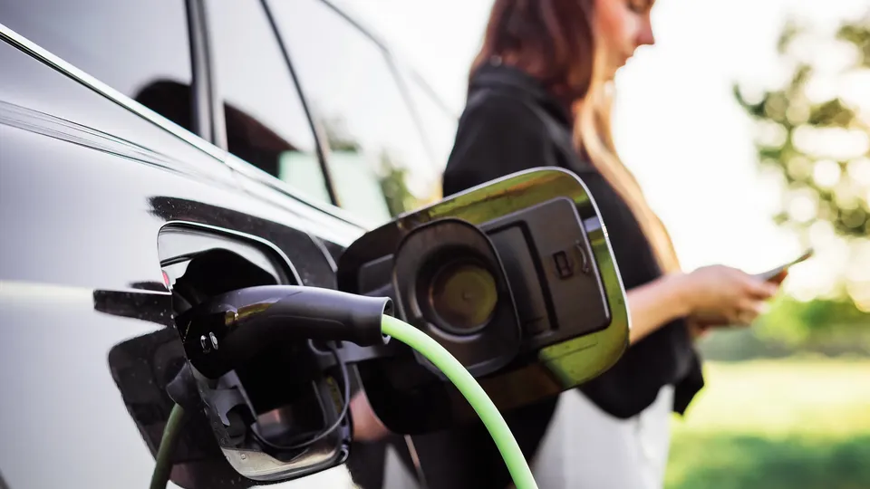 A person in a black top leaning against their EV while it charges