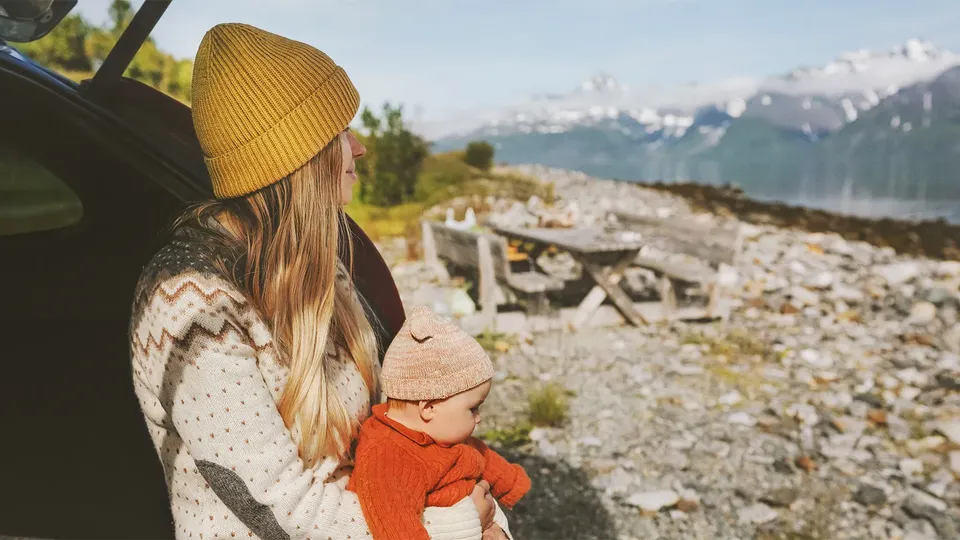 Kvinde holder småbarn og kigger på bjerglandskab fra en bil.