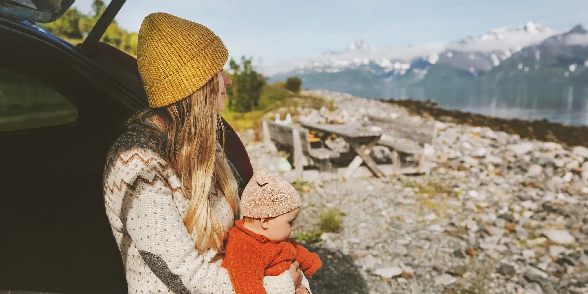 Kvinde holder småbarn og kigger på bjerglandskab fra en bil.
