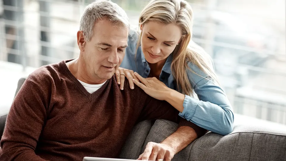 Ældre mand og kvinde ser på tablet sammen på sofa.