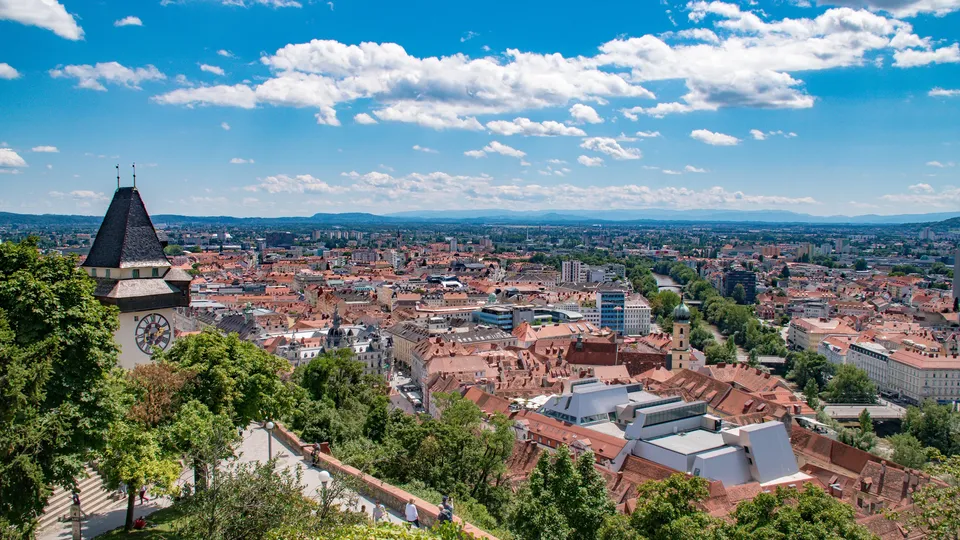 Panoramablick über Graz mit dem Uhrturm und der historischen Altstadt unter blauem Himmel.