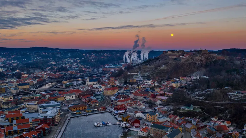 Halden by ved solnedgang med industrielle skorsteiner, havn og festning på toppen av bakke.