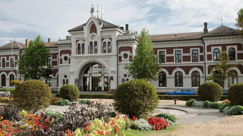 en liten bypark med den store historiske togstasjonen til Hamar i bakgrunnen.