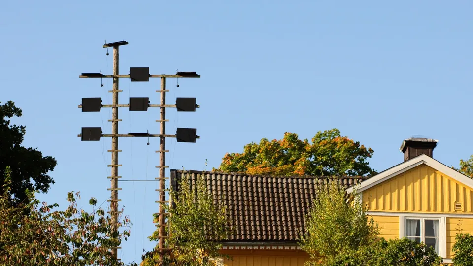 Gult trähus med elstolpar och ledningar i ett villaområde.