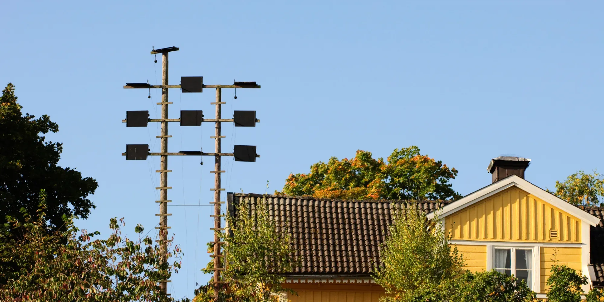 Gult trähus med elstolpar och ledningar i ett villaområde.