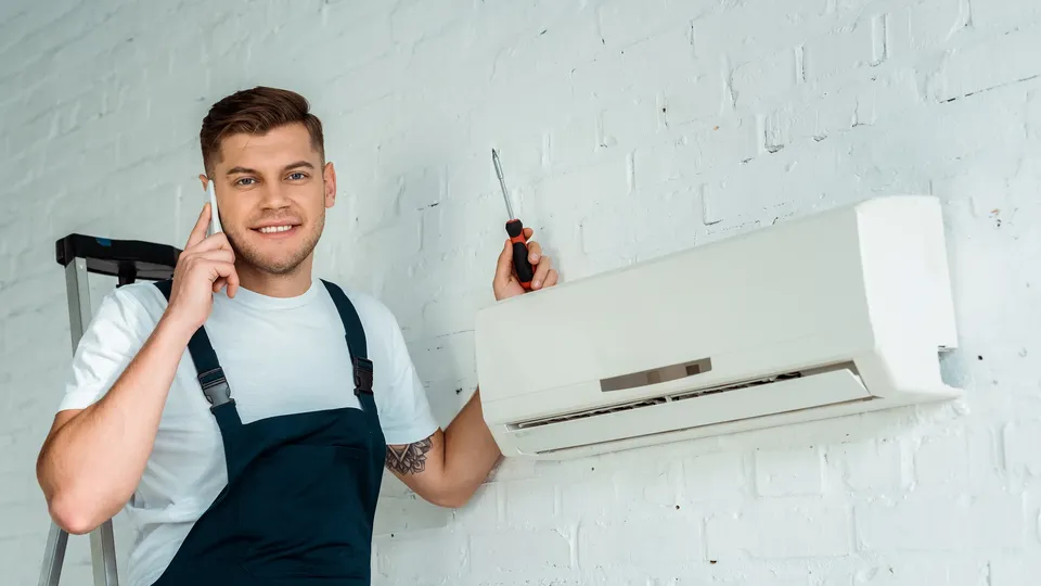 Tekniker holder skrutrekker mens han installerer varmepumpe på vegg.