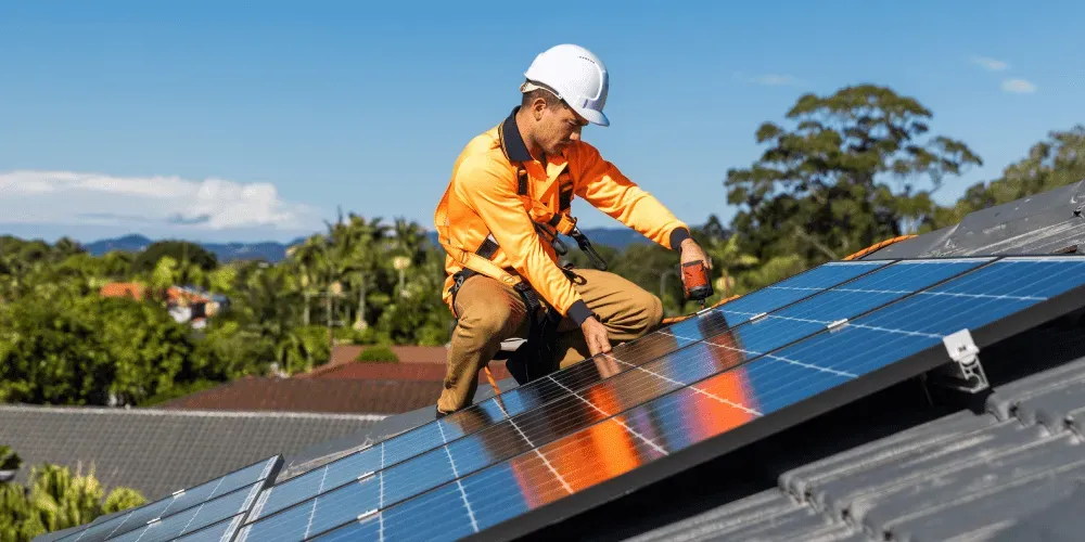 Worker in safety gear installing solar panels on a roof.