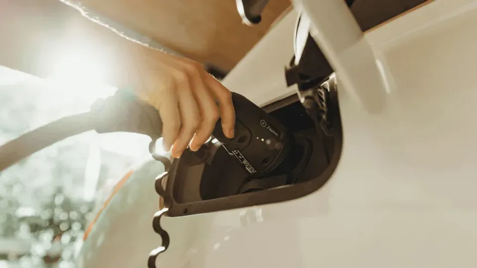 Hand plugging EV charging cable into electric vehicle port.