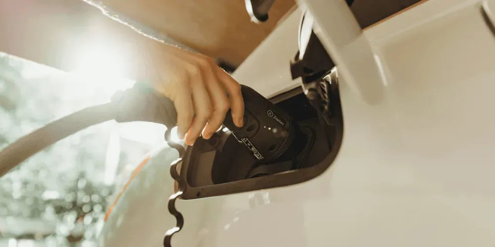 Hand plugging EV charging cable into electric vehicle port.