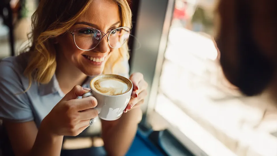 Kvinde holder kaffekop og smiler til en anden person.