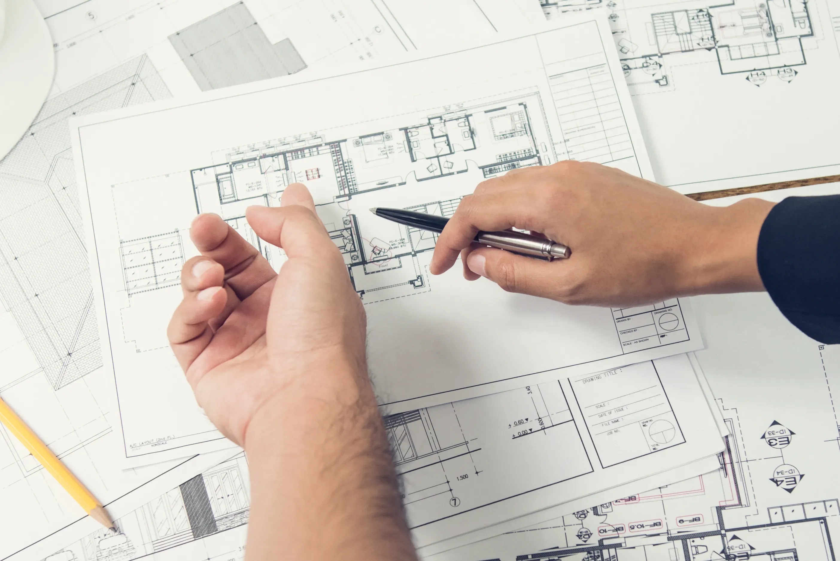 Arkitekt peker på plantegning med penn mens han gjennomgår blueprint.