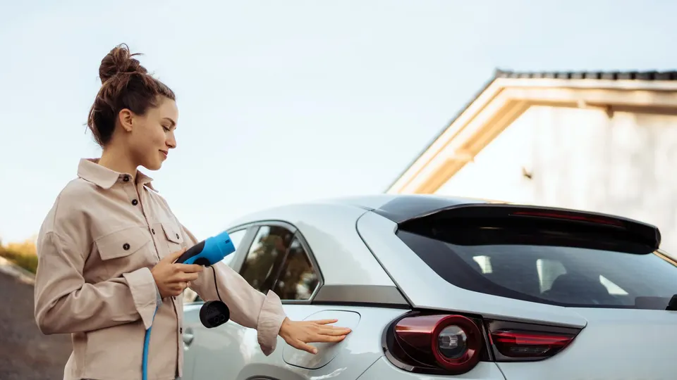 Bilde av ei dame som lukker opp ladeluka på bilen og holder en elbillader i hånda
