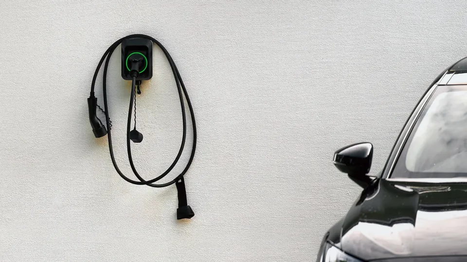 Elektrisk køretøjsopladningsstation monteret på hvid væg med sort kabel rullet op nedenfor.