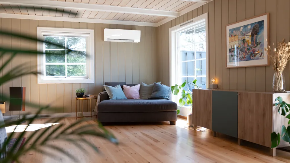 Veggmontert varmepumpe i moderne stue med sofa og planter.